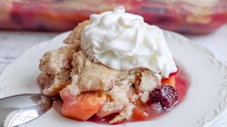 Portion of blackberry peach cobbler on plate, topped with whipped cream