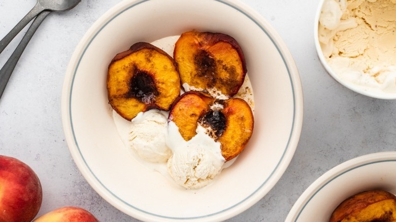 Baked peaches in bowl with scoops of vanilla ice cream