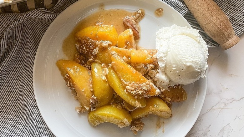 Portion of peach crisp with scoop of vanilla ice cream on plate