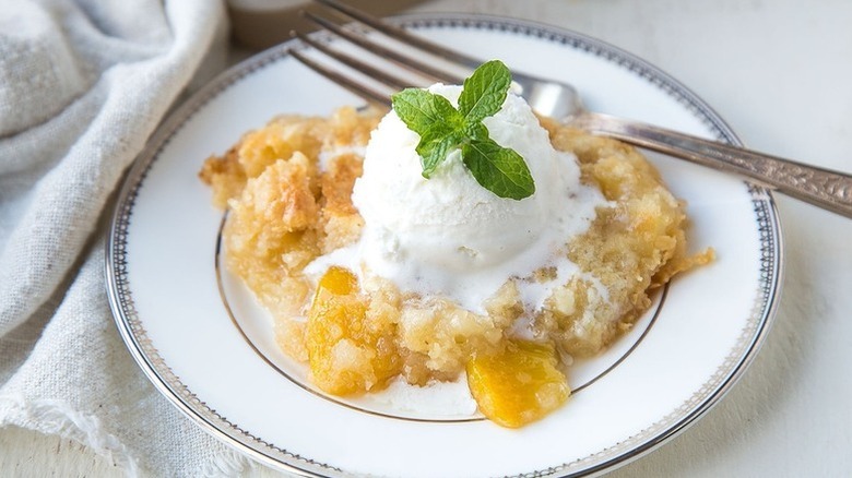Portion of peach dump cake on plate, topped with scoop of ice cream and sprig of mint