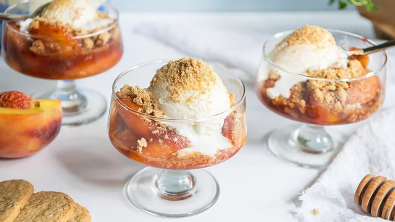 Peach crumble topped with scoops of ice cream served in dessert glasses