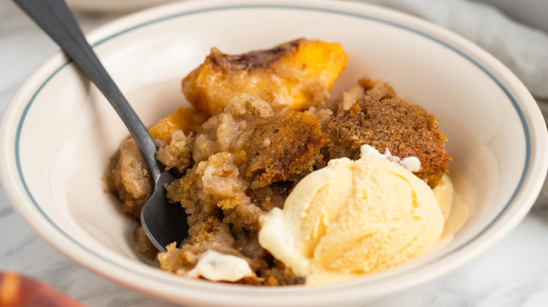 Portion of peach pudding on bowl with scoop of vanilla ice cream
