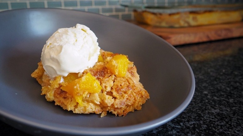 Portion of peach cobbler on plate, topped with scoop of vanilla ice cream