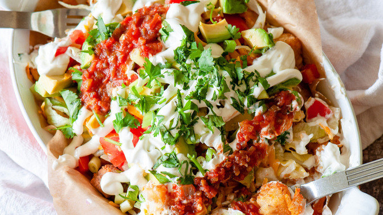 Totchos in baking dish, topped with sour cream, salsa, and cilantro