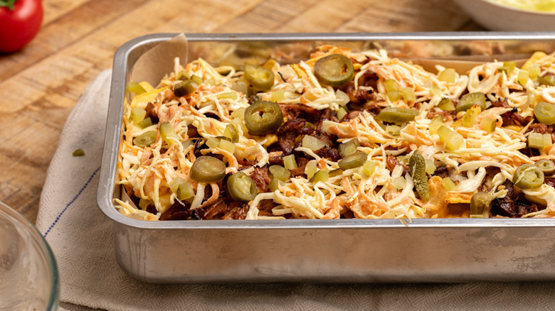 Pulled pork nachos in roasting tin, topped with sliced jalapenos and pickles