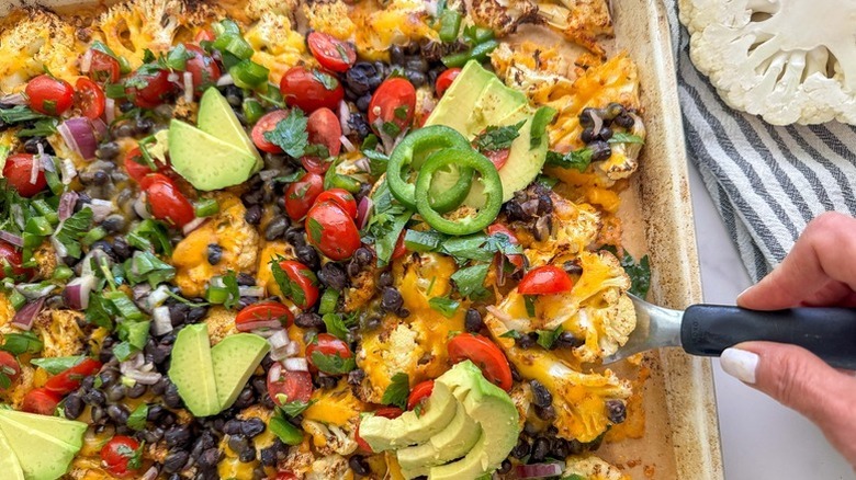 Cauliflower nachos on sheet pan, topped with avocado, tomatoes, and olives