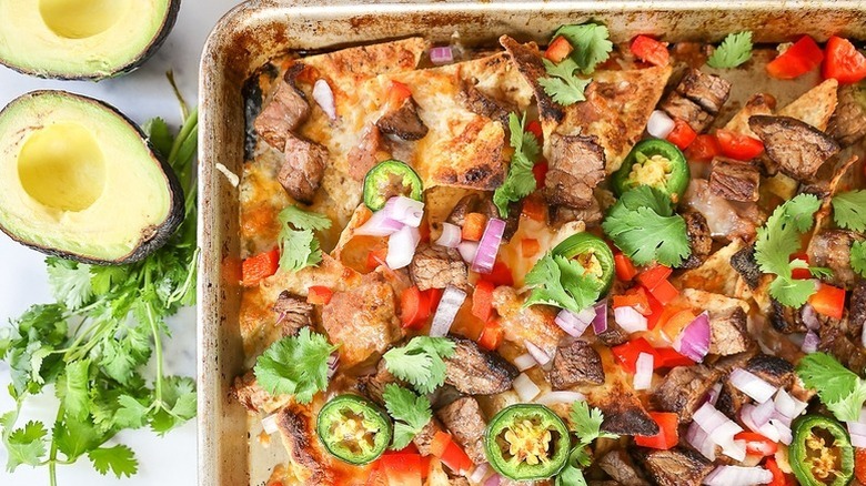 Nachos in sheet pan, topped with steak, jalapenos, red onion, and tomatoes