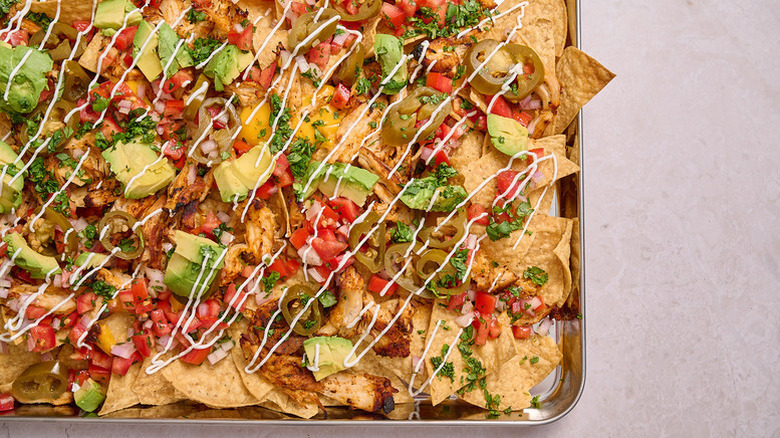 Sheet pan nachos topped with chicken, avocado, and tomatoes