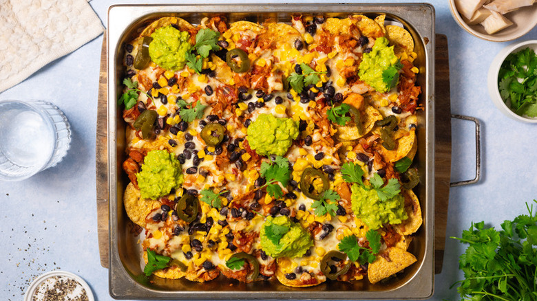 Jackfruit nachos in roasting tin, topped with guacamole, cilantro, and jalapeno slices