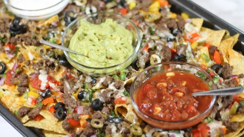 Sheet pan nachos with bowls of guacamole, salsa, and sour cream