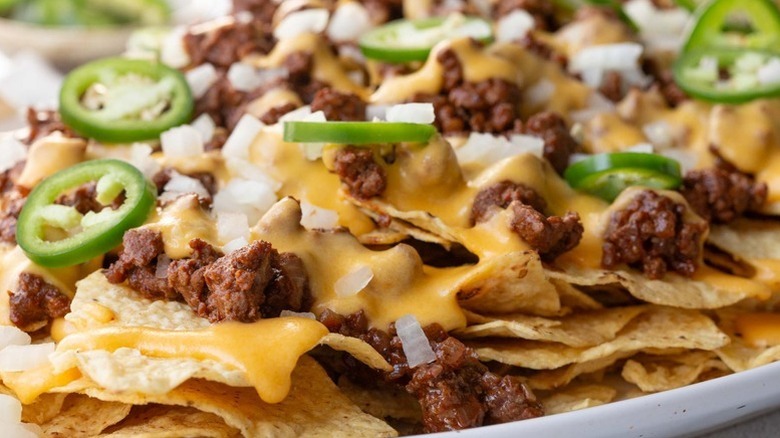 Close up of nachos topped with ground beef, cheese sauce, diced onions, and jalapeno slices