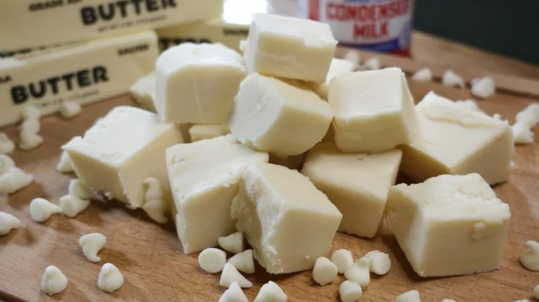 A small pile of white chocolate fudge cubes on a wood board with white chocolate chips