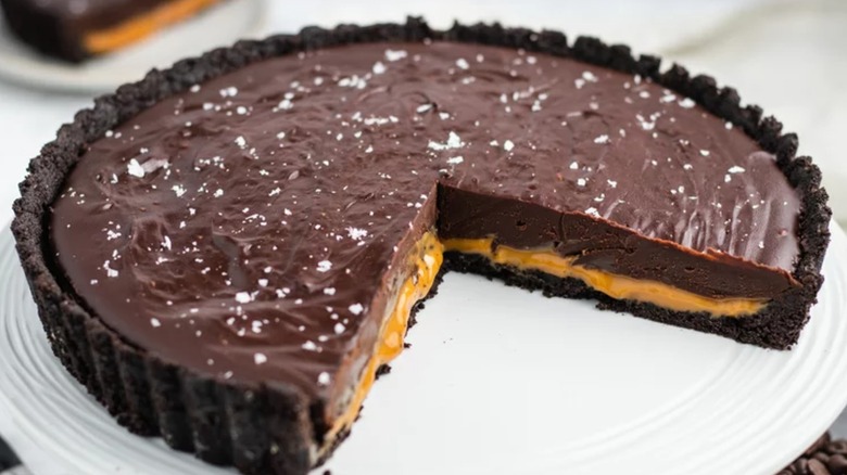 A chocolate caramel tart with flakey sea salt on top on a white dish