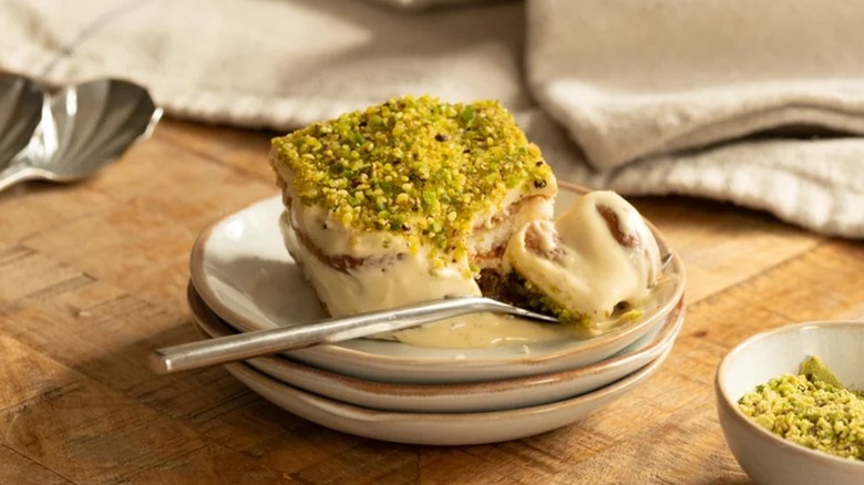 A slice of pistachio tiramisu on stacked white plates with a spoon