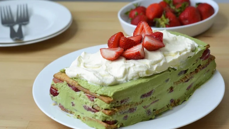 A strawberry matcha icebox cake on a white plate with a bowl of strawberries in the background
