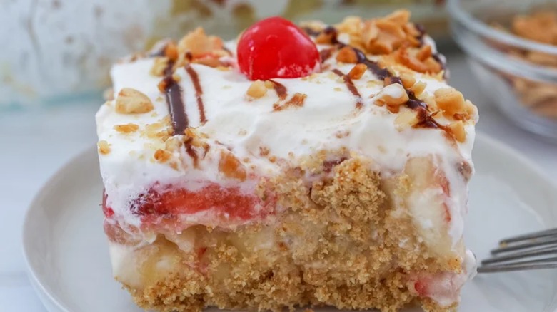 A close-up of a slice of banana split cake with a cherry on top