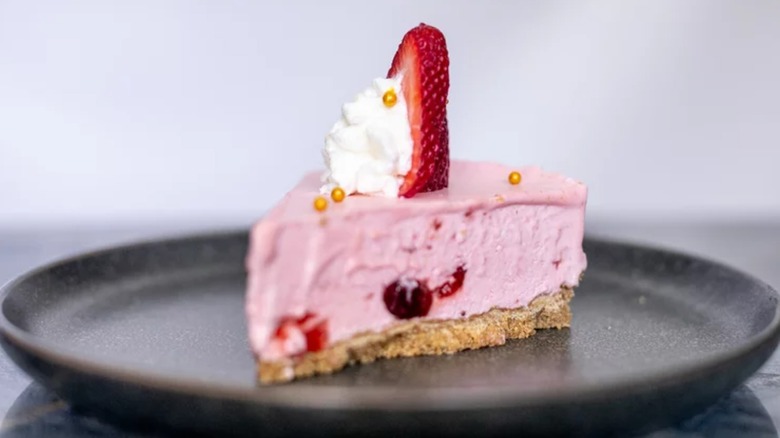A small slice of strawberry cheesecake on a black plate