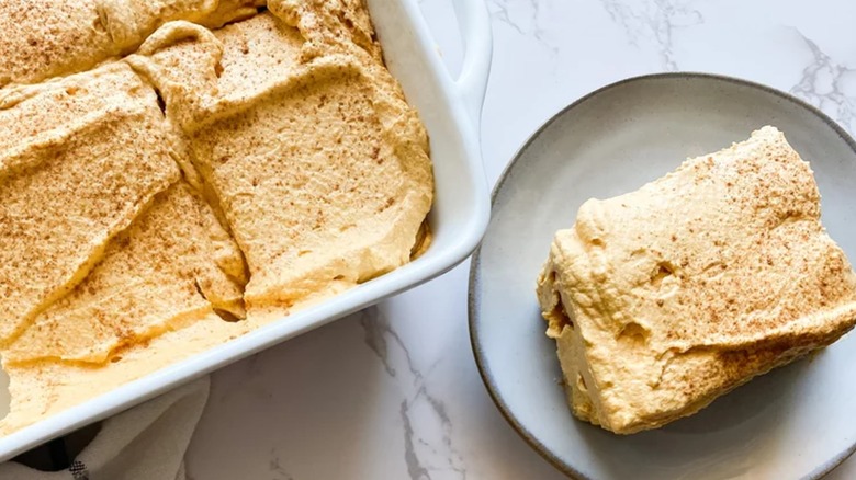 A slice of pumpkin tiramisu on a plate next to the rest of the dessert in a large dish