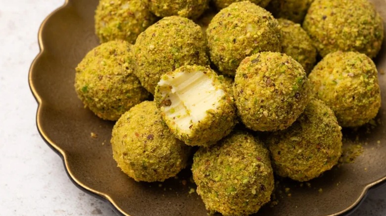 A pile of pistachio white chocolate truffles on a plate with a bite taken out of one