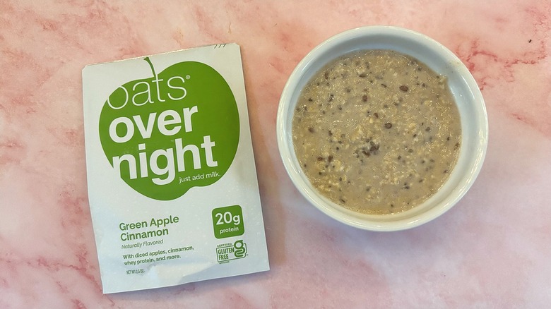 Bowl of Oats Overnight Apple Cinnamon next to packet on pink surface