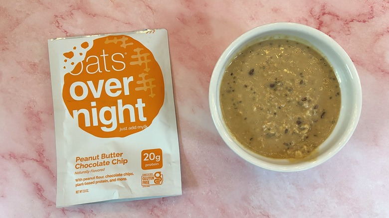 Bowl of Oats Overnight Peanut Butter Chocolate Chip next to packet on pink surface