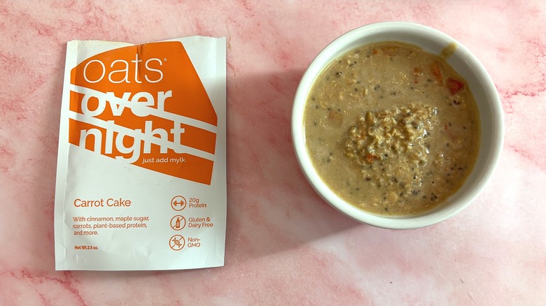 Bowl of Oats Overnight Carrot Cake next to packet on pink surface