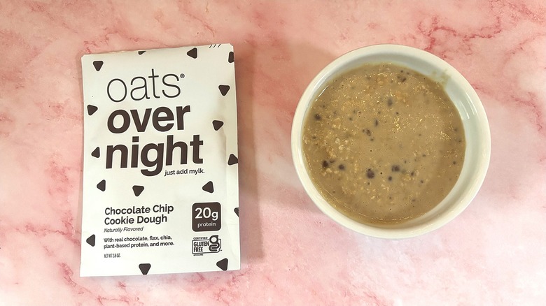 Bowl of Oats Overnight Chocolate Chip Cookie Dough next to packet on pink surface