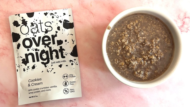 Bowl of Oats Overnight Cookies & Cream next to packet on pink surface