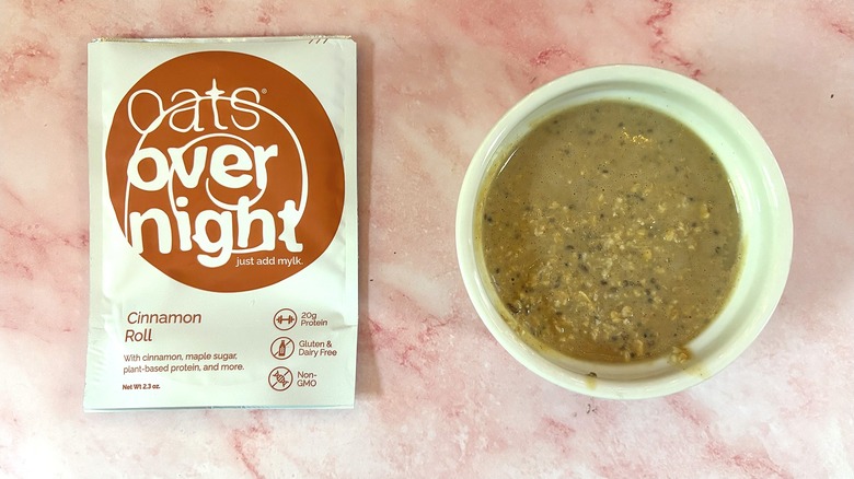 Bowl of Oats Overnight Cinnamon Roll next to packet on pink surface