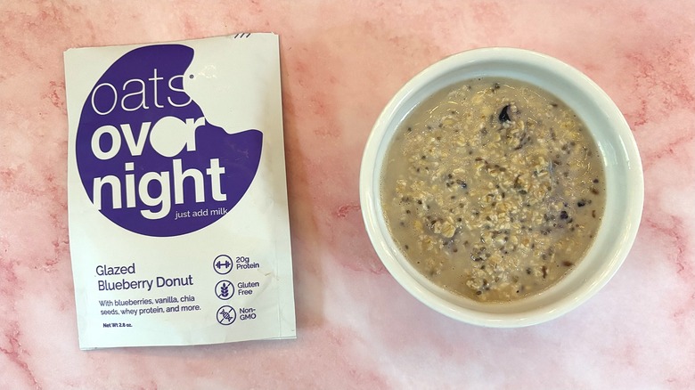 Bowl of Oats Overnight Glazed Blueberry Donut next to packet on pink surface