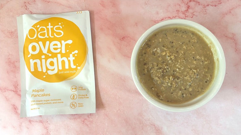 Bowl of Oats Overnight Maple Pancakes next to packet on pink surface
