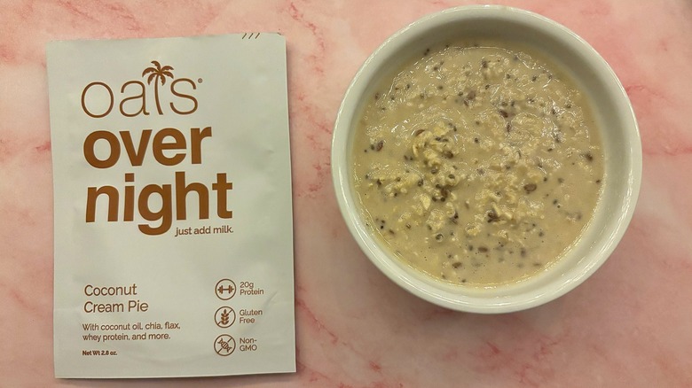 Bowl of Oats Overnight Coconut Cream Pie next to packet on pink surface