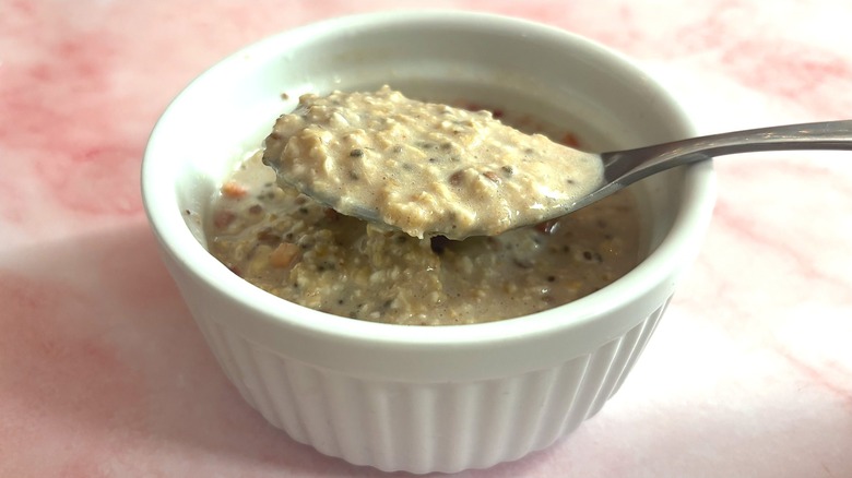 Spoon with some Oats Overnight over cup of oats on pink surface