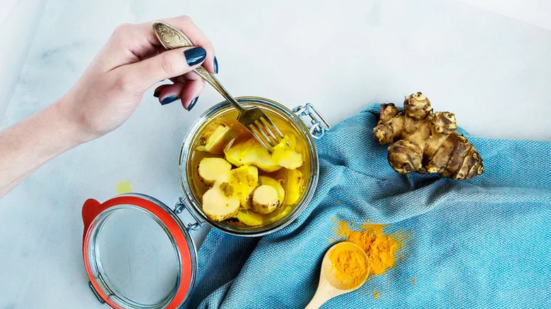 Hand using fork to grab Bread and Butter Pickled Sunchokes in glass jar