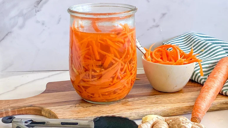 Gingery Pickled Carrots in glass jar on wooden cutting board