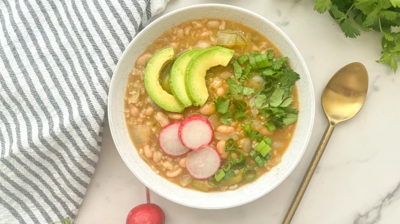 Bowl of white bean chili with avocado and radish garnishes