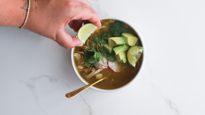 Hand squeezing lime into bowl of chicken posole verde soup