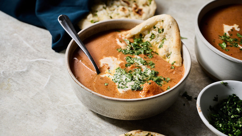 Chicken tikka masala soup in bowl with naan bread and chopped cilantro garnish