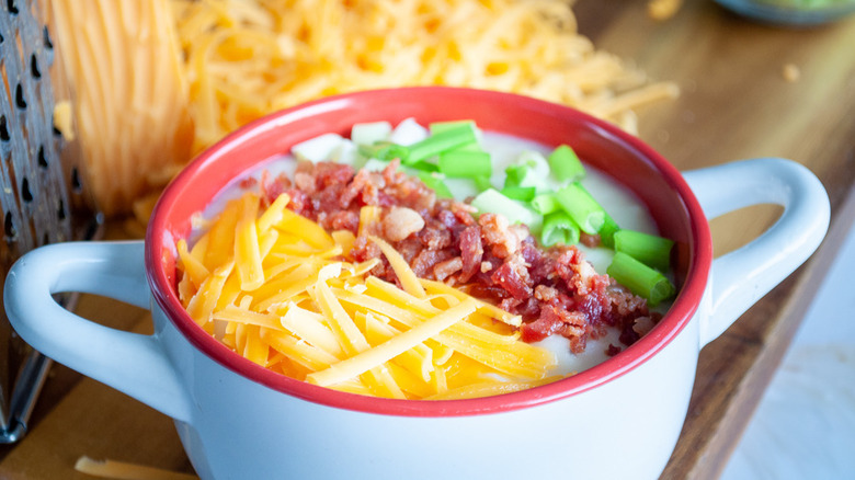 Bowl of potato soup topped with grated cheese, crumbled bacon, and chopped green onion
