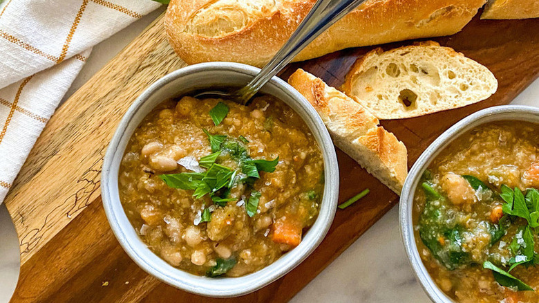 Two bowls of white bean soup next to crusty baguette