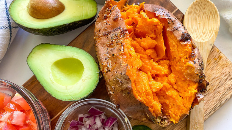 Baked sweet potato on wooden board next to halved avocado