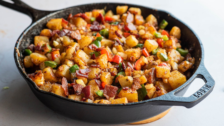 Fried cubed potatoes in skillet with bacon and bell peppers