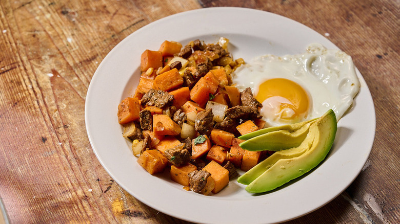 Steak and sweet potato hash on plate with fried egg and sliced avocado