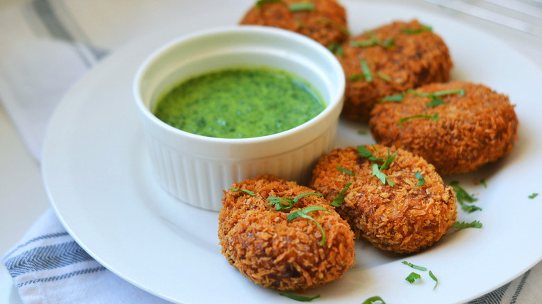 Spicy sweet potato and lentil croquettes on plate with bowl of green dip and a herby garnish