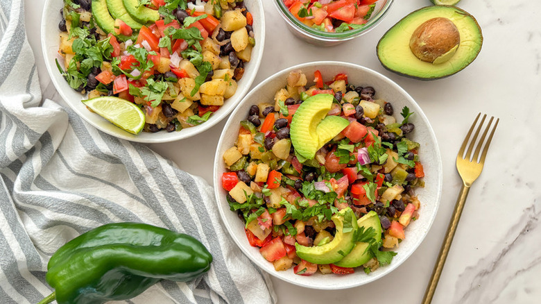 Top view of pepper and potato hash in bowls, topped with avocado slices and fresh cilantro