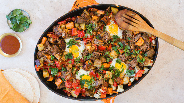 Top view of sweet potato and brisket hash with eggs in large skillet with wooden spoon