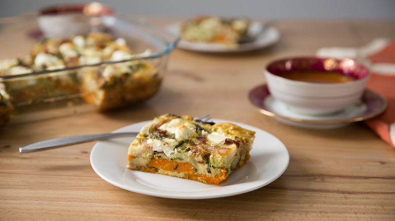 Slice of sweet potato breakfast casserole on plate with the whole dish in the back