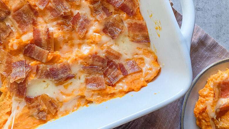 Close up of cheesy sweet potato and bacon casserole in white dish