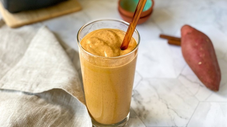 Sweet potato smoothie in glass with straw on a marble counter with sweet potato in the background