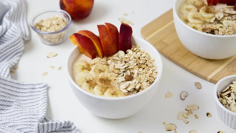 Creamy Peach Almond Smoothie Bowl in white bowl surrounded by ingredients
